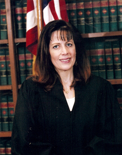 Portrait of The Honorable Deborah Kaplan in chambers with flag and bookcase in the background